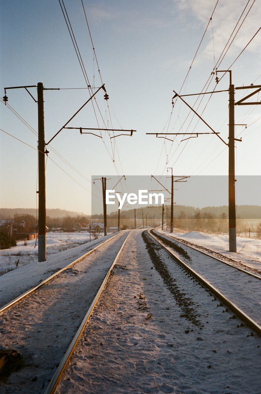 Diminishing perspective of snow covered railroad tracks against sky during sunset