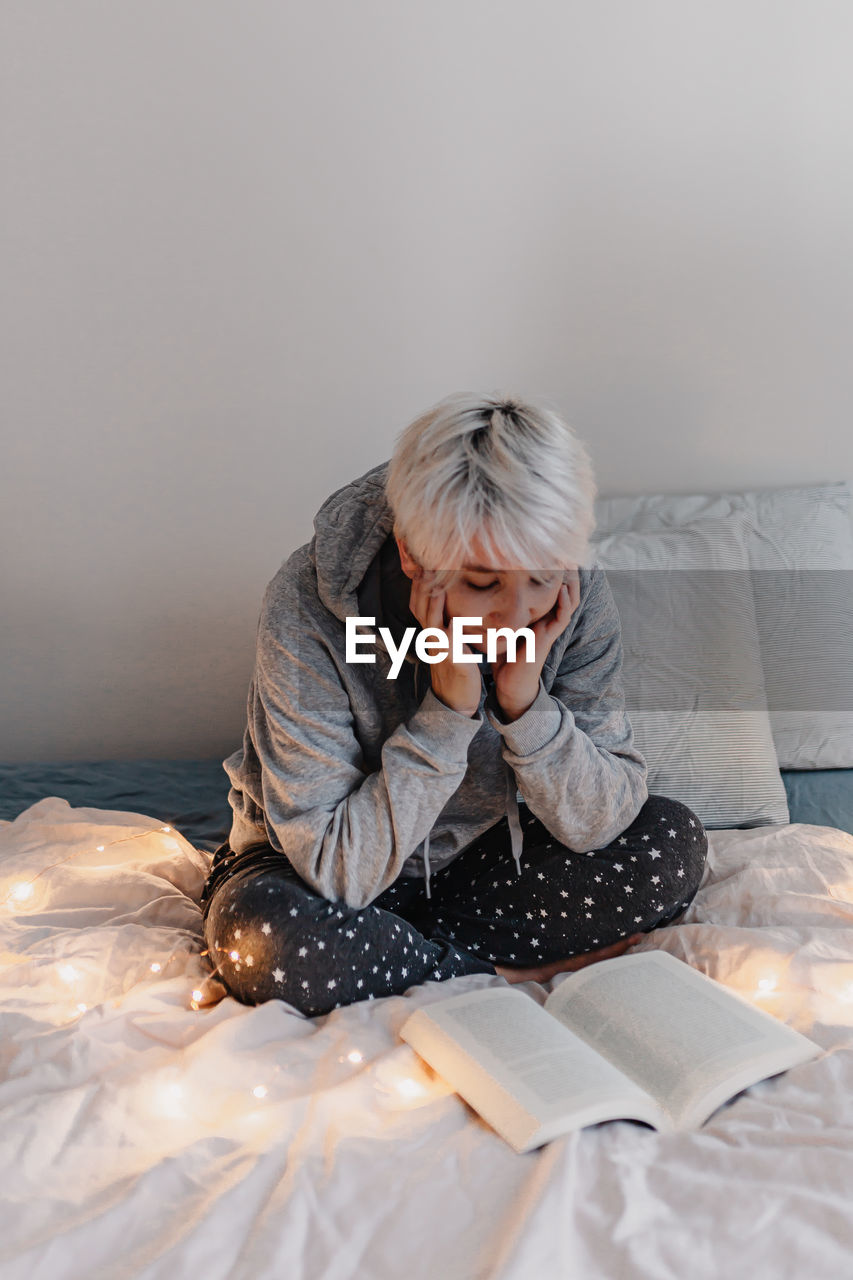 Woman sitting on bed while reading book at home