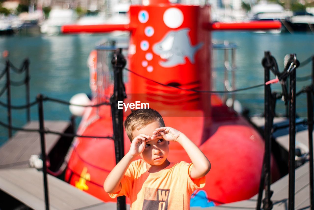 Cute boy shielding eyes while looking away at harbor