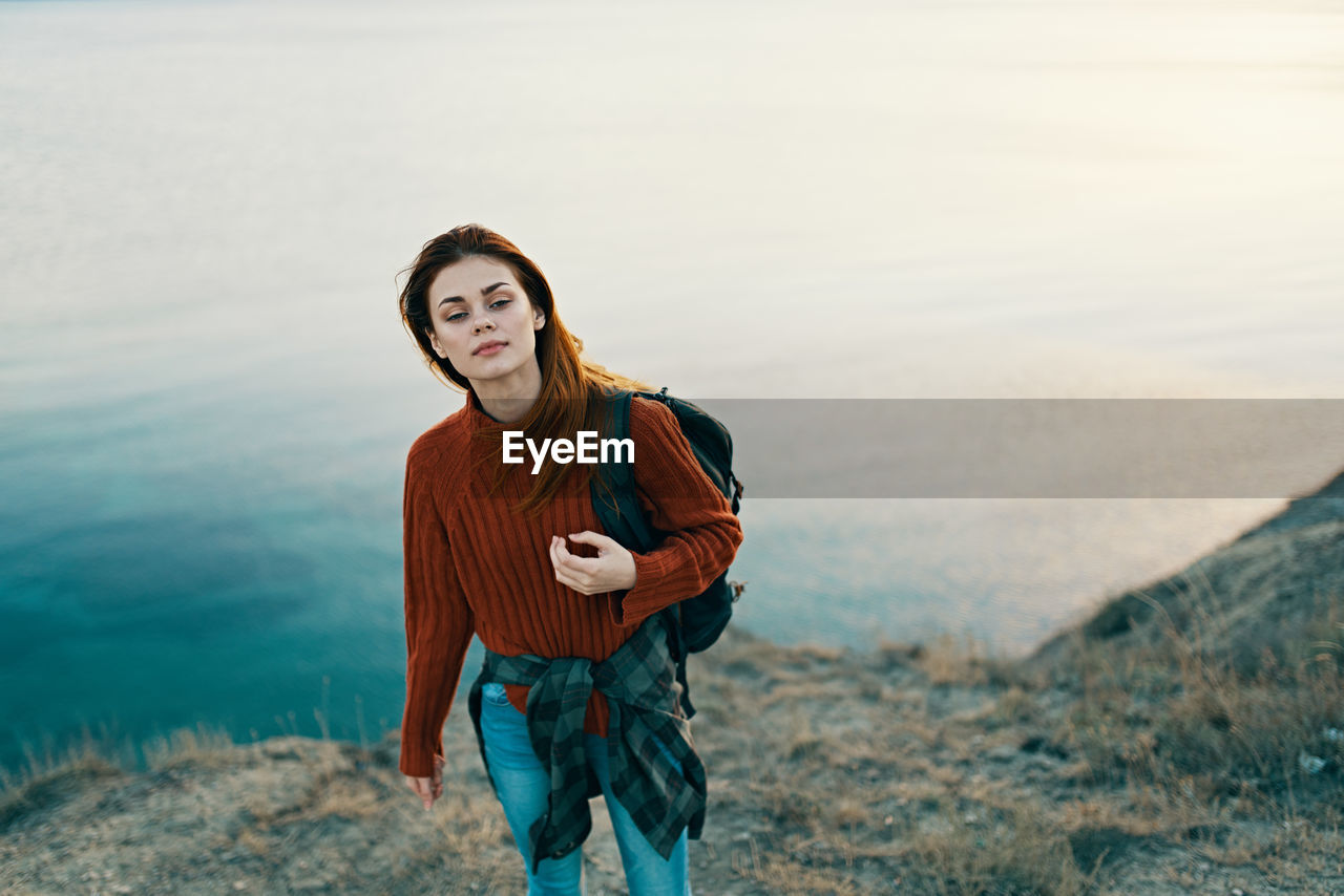 PORTRAIT OF BEAUTIFUL YOUNG WOMAN STANDING AGAINST WATER