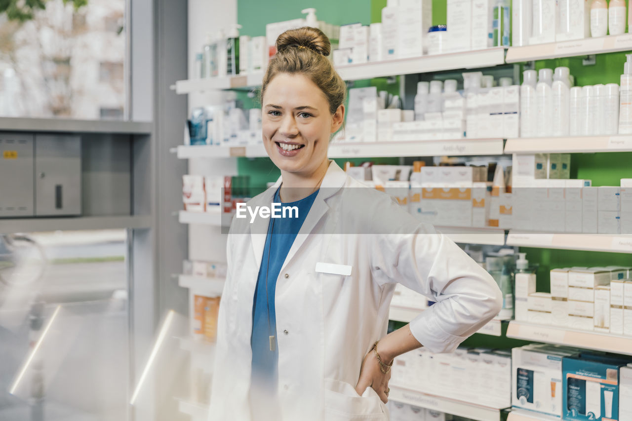 Happy pharmacist with hand on hip standing in chemist shop