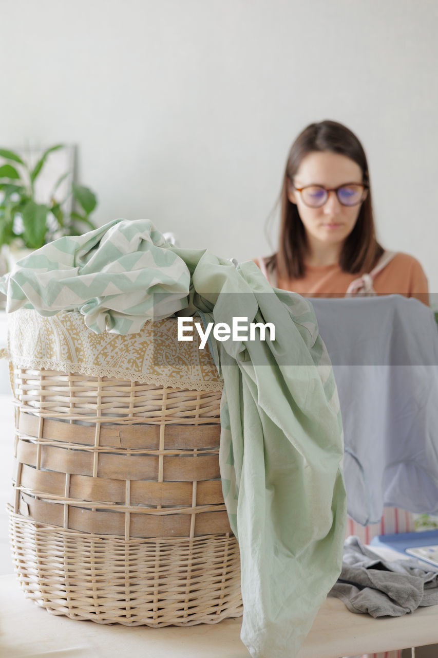 portrait of young woman in wicker basket on table against wall