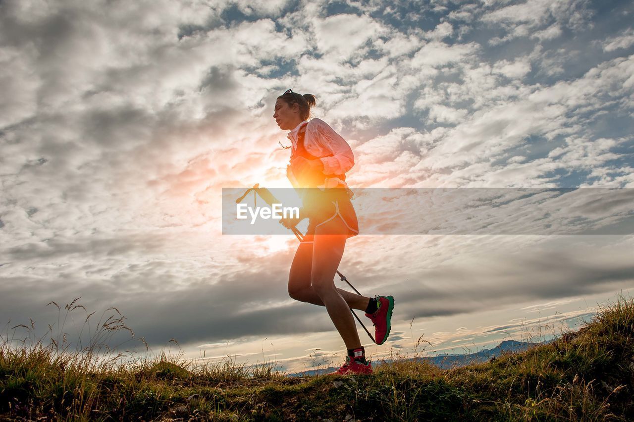 Low angle view of young woman jumping against sky during sunset