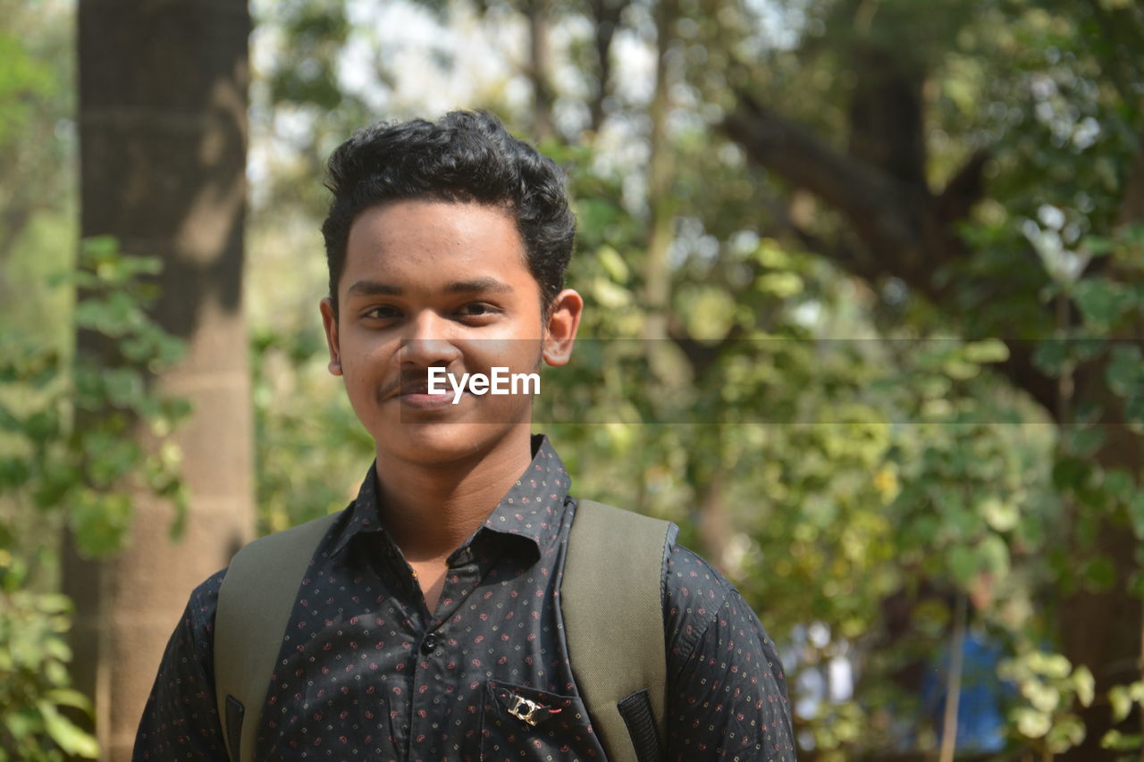 Portrait of young man standing against trees