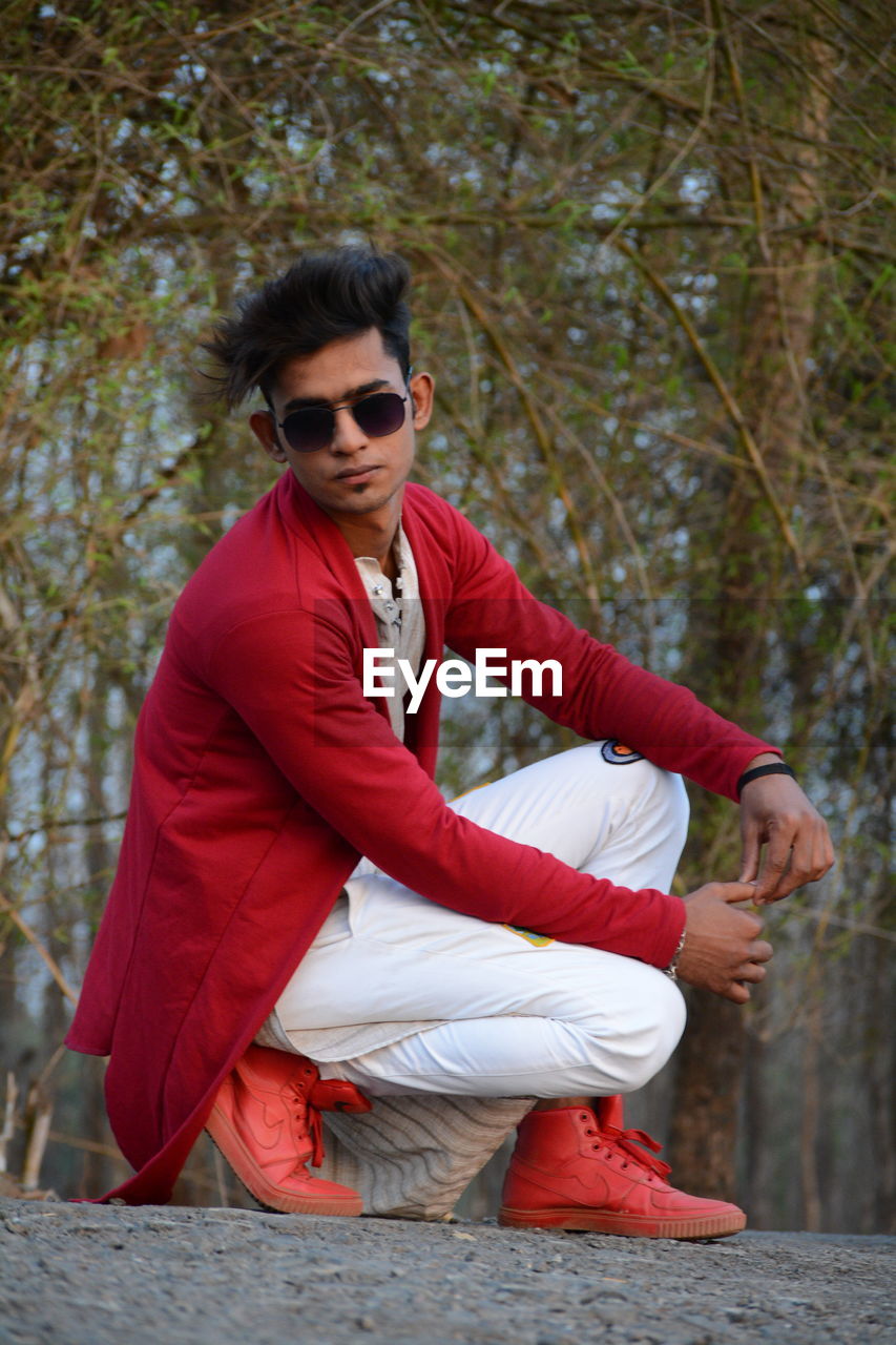 Young man wearing sunglasses sitting on tree