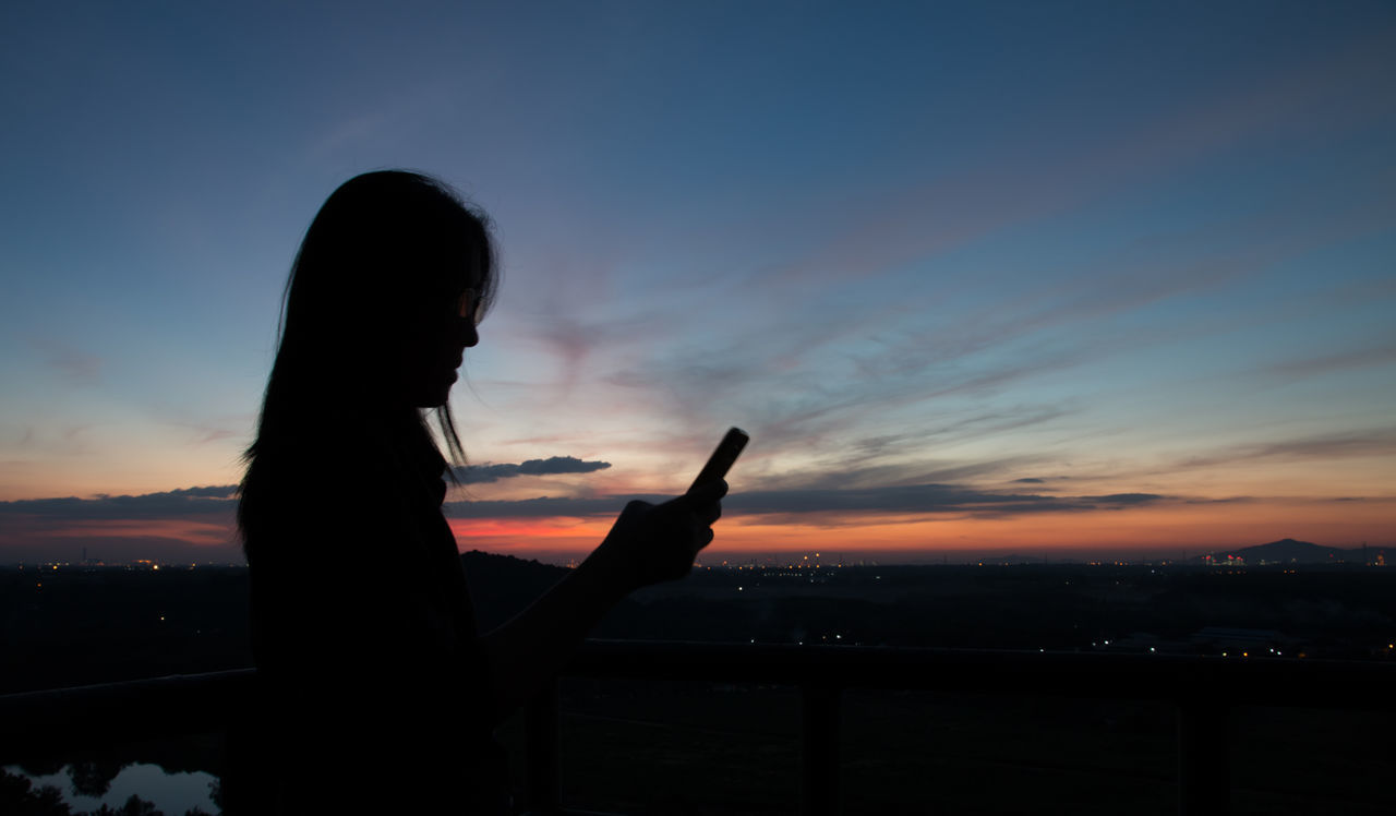 Silhouette woman using mobile phone during sunset