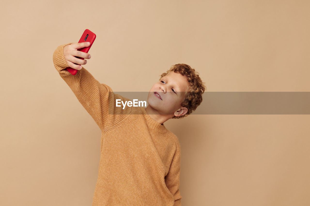 Boy taking selfie against beige background