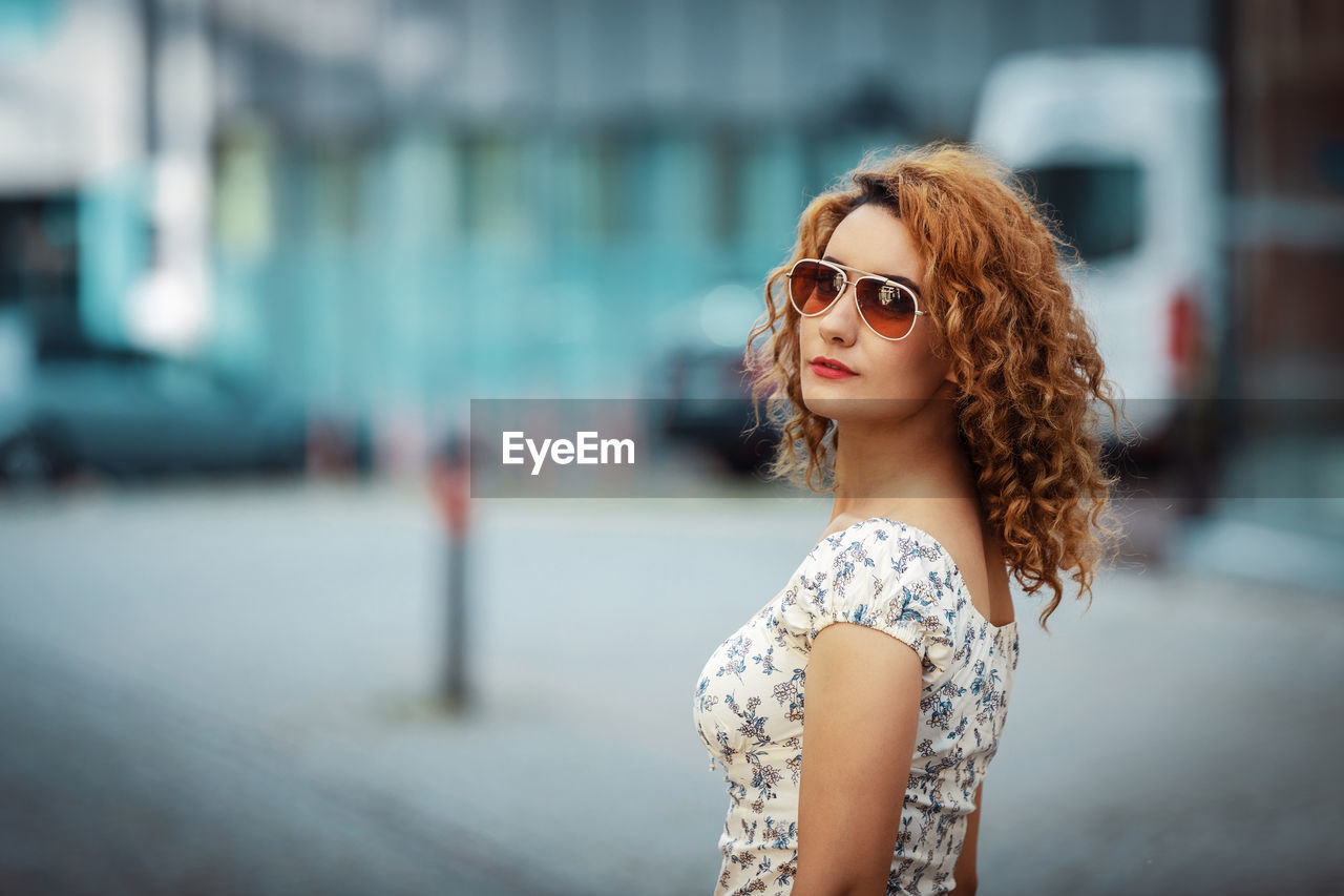 Young moroccan woman with curly hair, wearing sunglasses, turning to camera, in urban environment 