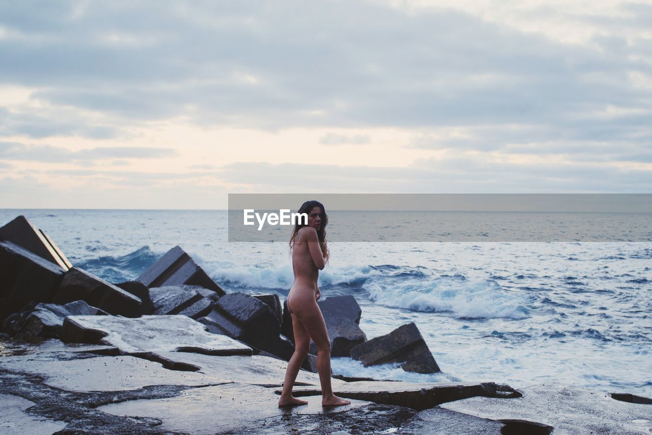 Portrait of naked woman standing on rock at beach