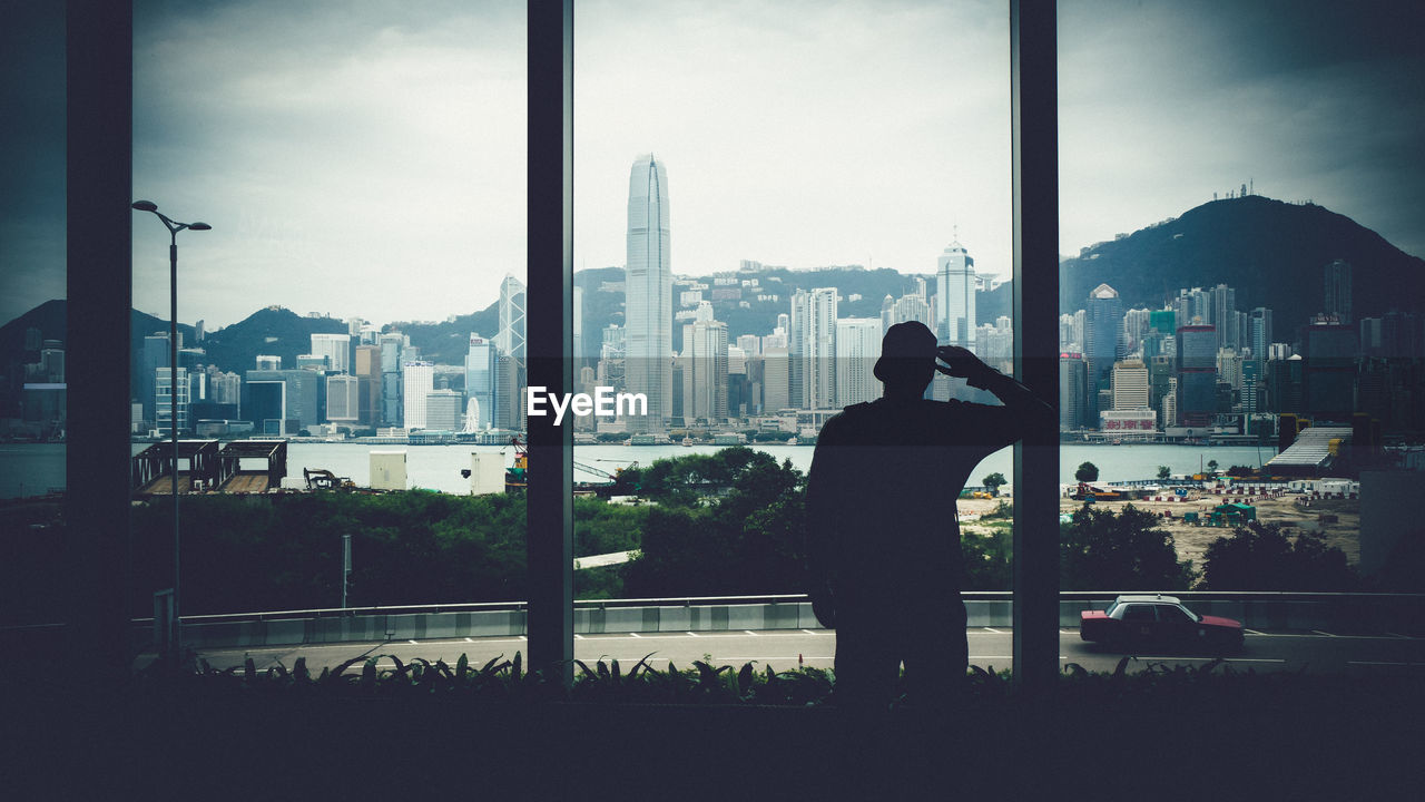 Silhouette man standing by window against victoria harbour