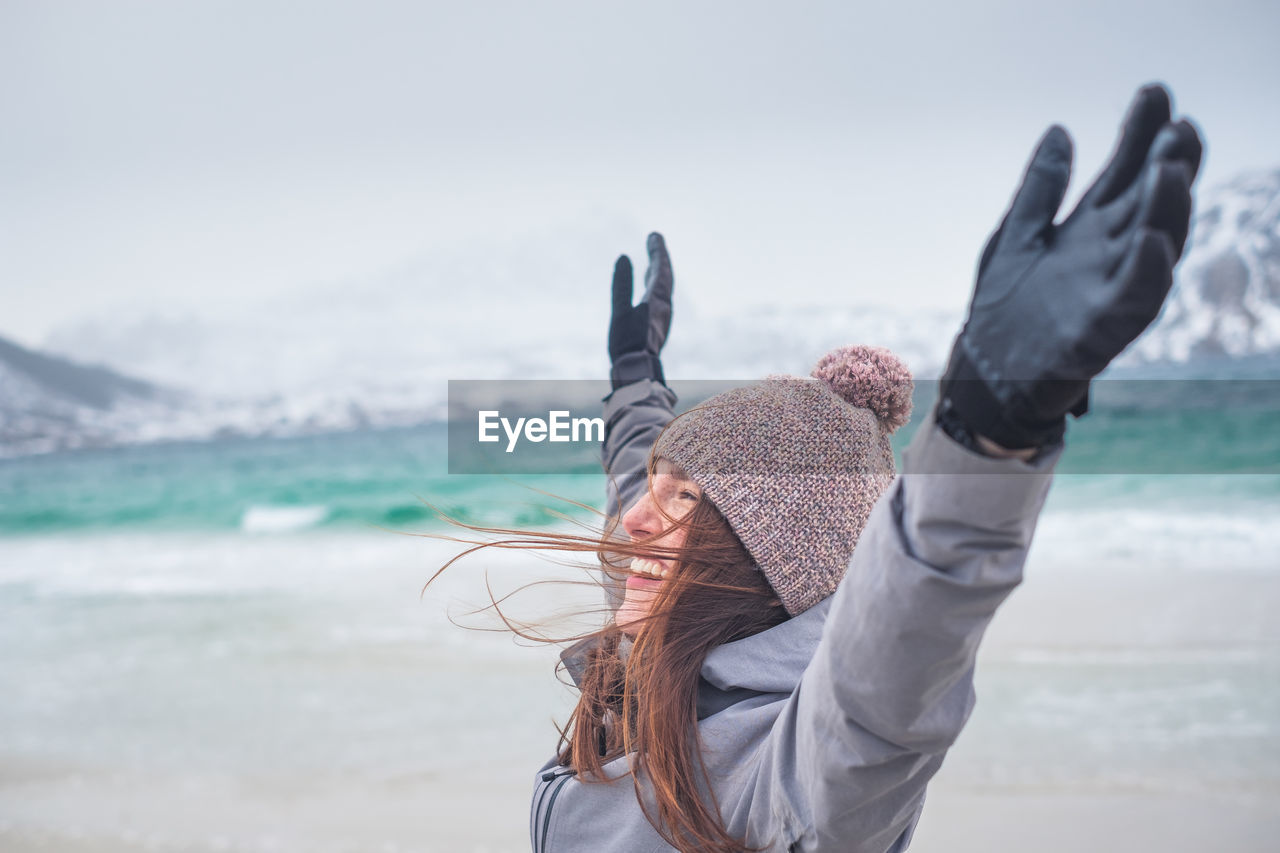 Smiling woman with arms raised standing outdoors during winter