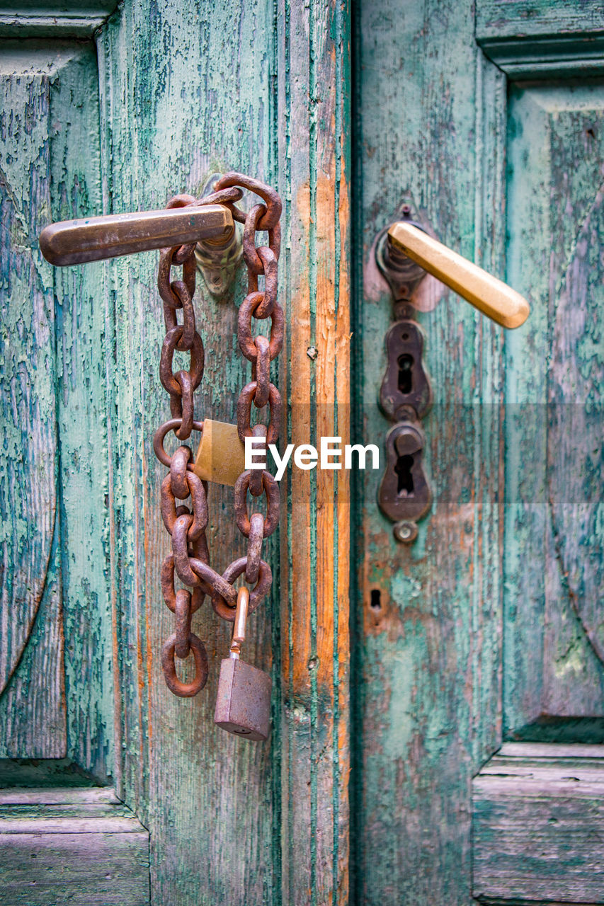 Close-up of old wooden door with rusty padlock and chain