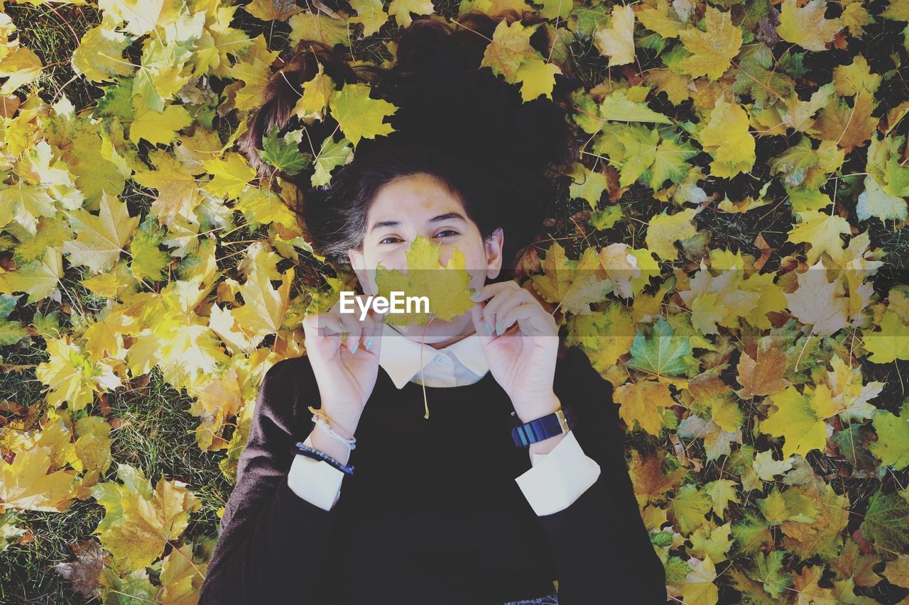 Portrait of woman holding autumn leaf against mouth