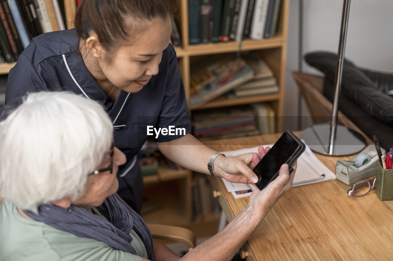 Home carer helping senior woman to use cell phone