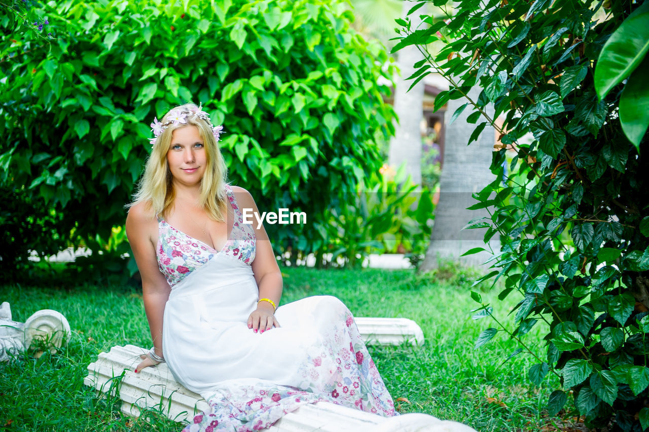 Portrait of young woman sitting against plants