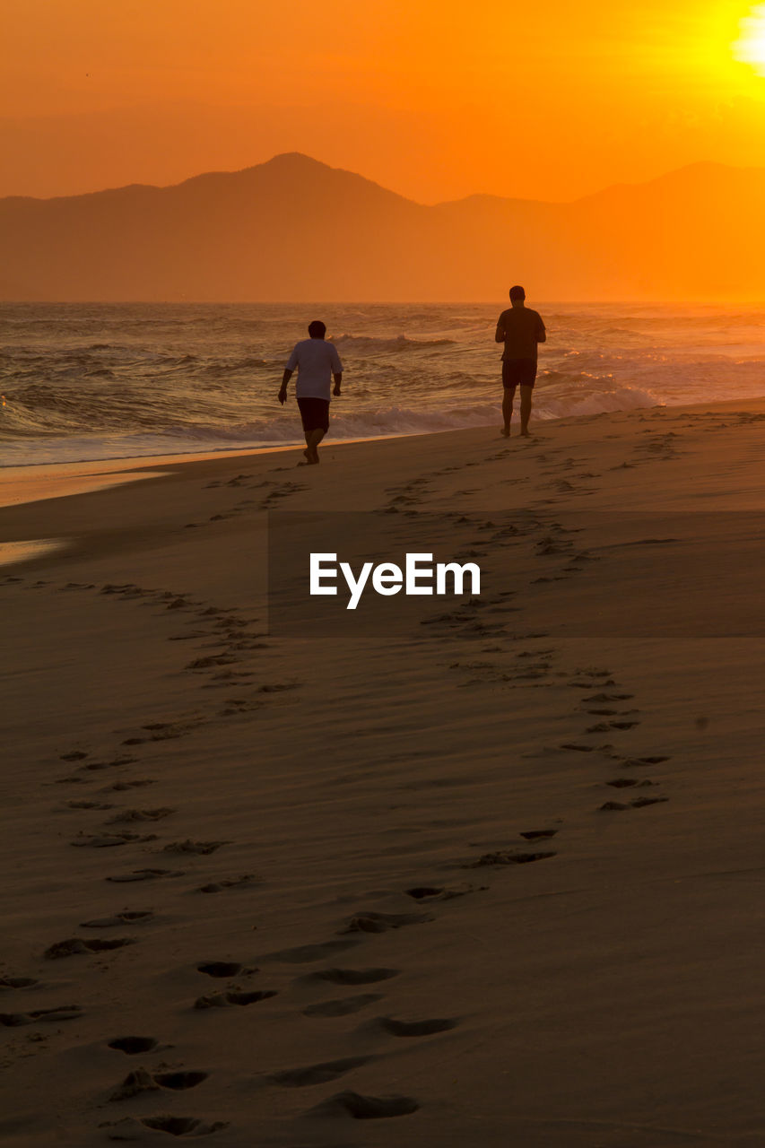 Silhouette people playing on beach against sky during sunset