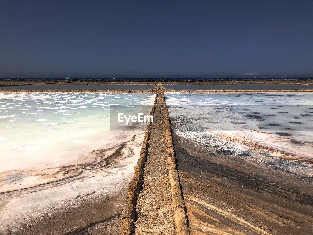 Scenic view of sea against clear sky and path across pink salt mine