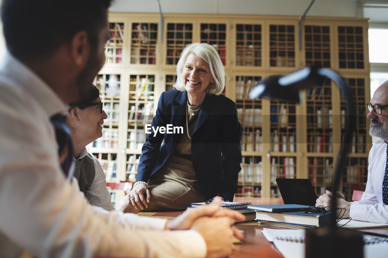 Happy senior lawyer sitting on table during meeting in library