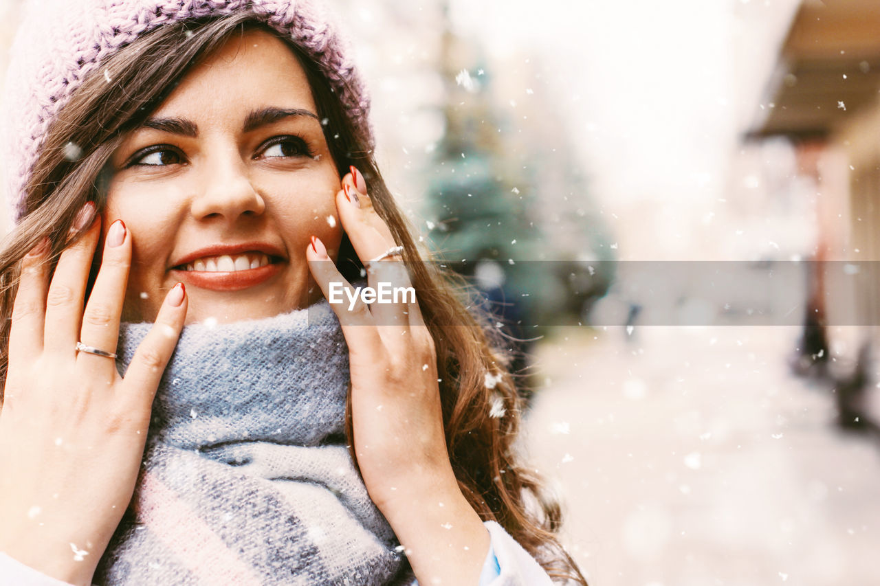 Close-up of young woman looking away while standing outdoors during snowfall