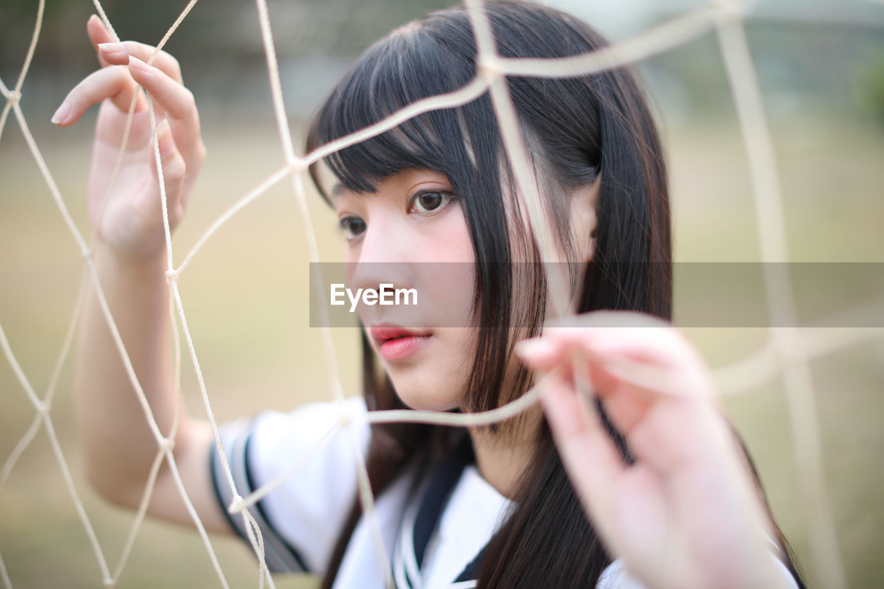 Young woman standing by net outdoors