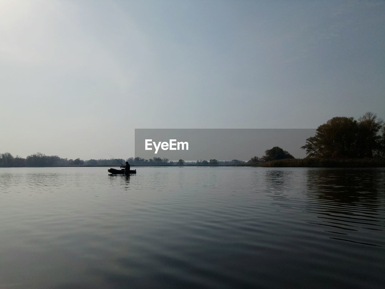 Scenic view of lake against sky with person fishing in background