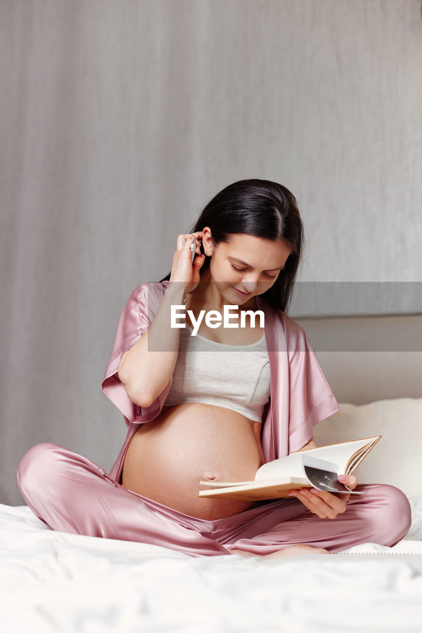 Pregnant woman writing on bed at home