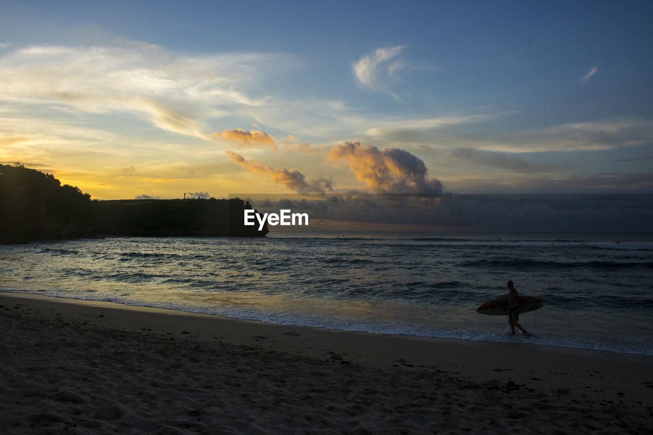 Man with surfboard at beach during sunset