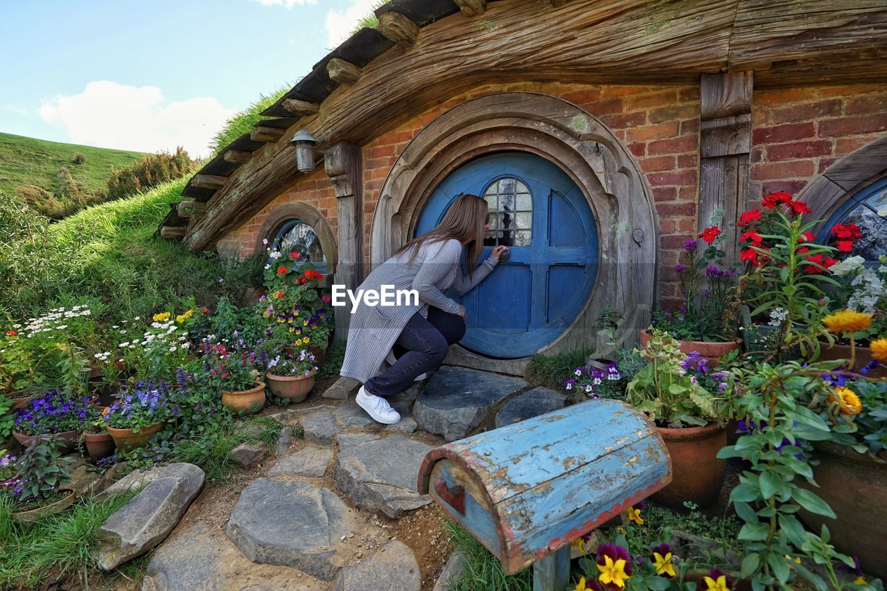 WOMAN STANDING BY FLOWERS AGAINST WALL