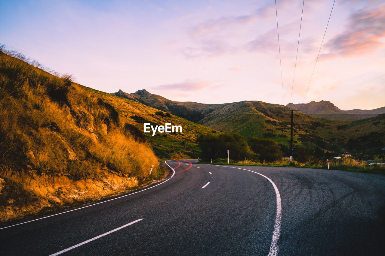 Road by mountains against sky during sunset