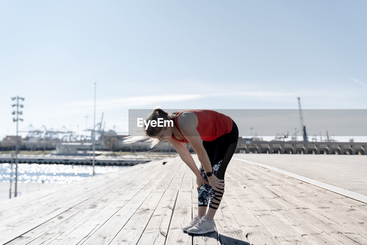 Young female athlete resting on pier during sunny day