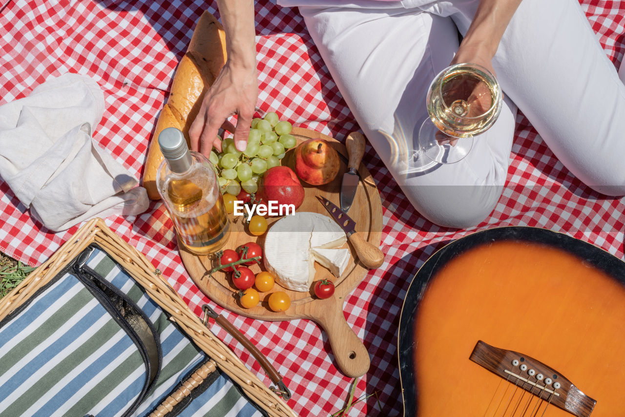 Top view of unrecognizable young woman in white pants outside having picnic, eating and playing