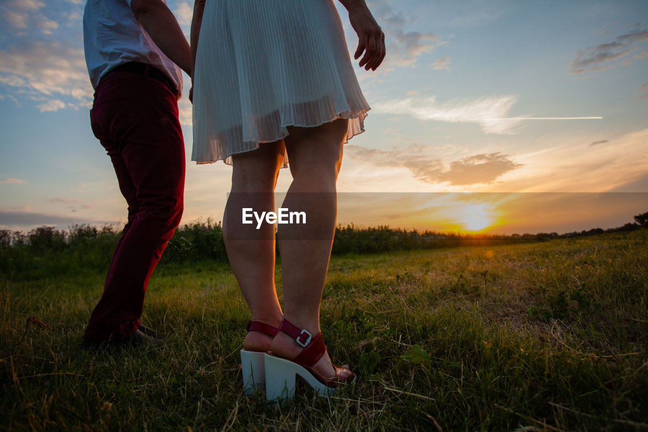 Low section of women standing on field against sky during sunset