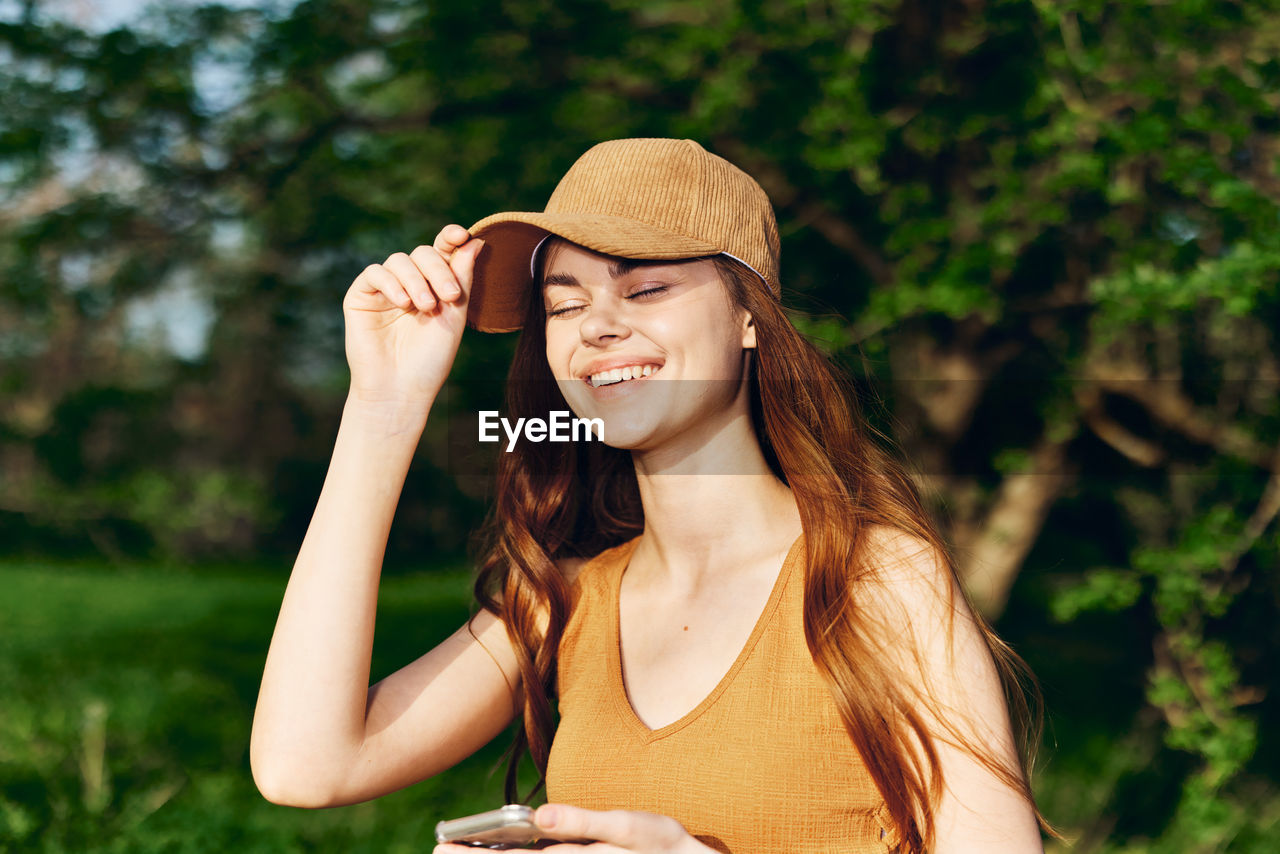 portrait of young woman wearing hat standing against plants