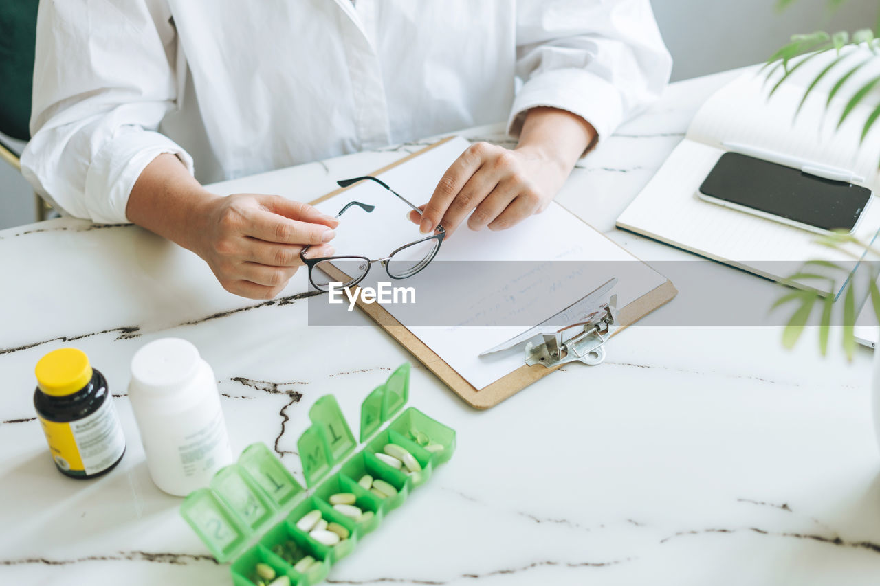 Crop photo of woman nutritionist doctor plus size in white shirt working at table with daily pills 