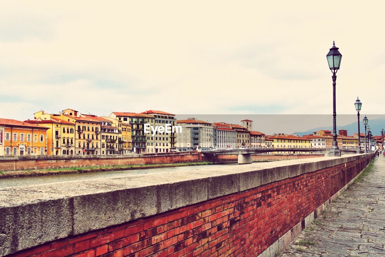 Retaining wall by river in city against sky