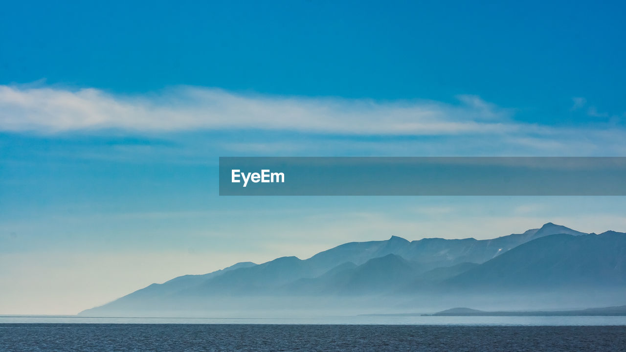 Scenic view of sea and mountains against blue sky