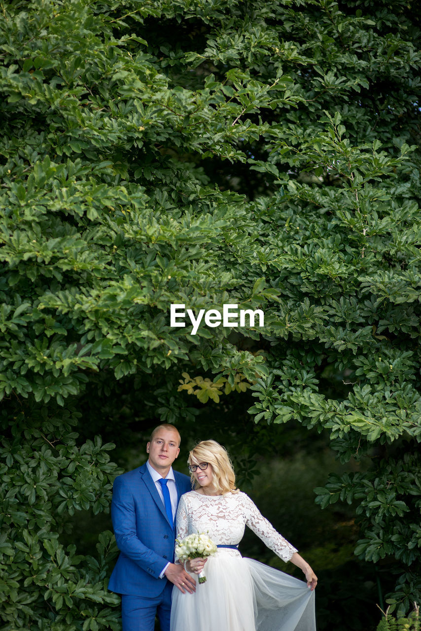 Portrait of bridal couple standing against tree branches at park