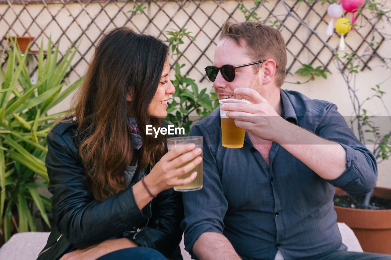 Couple toasting beer glasses while sitting outdoors