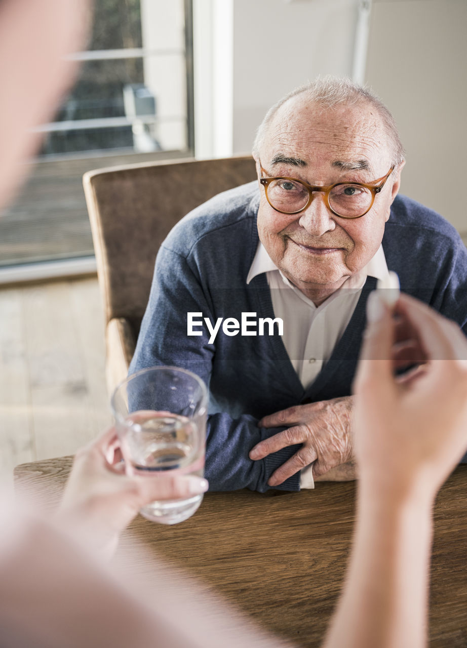 Woman holding pill and glass of water for smiling senior man