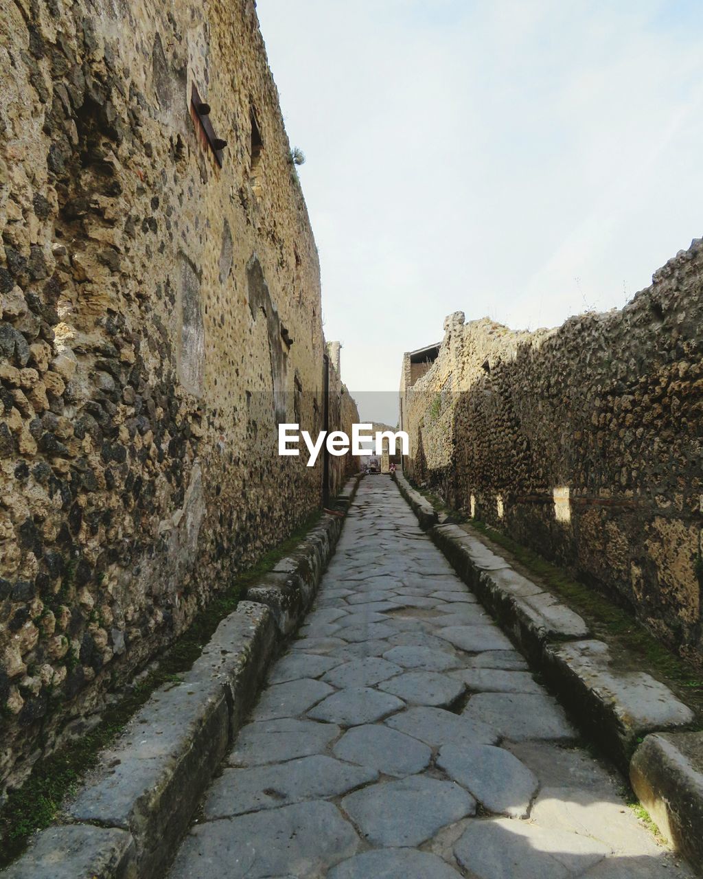 WALKWAY AMIDST BRICK WALL AGAINST SKY