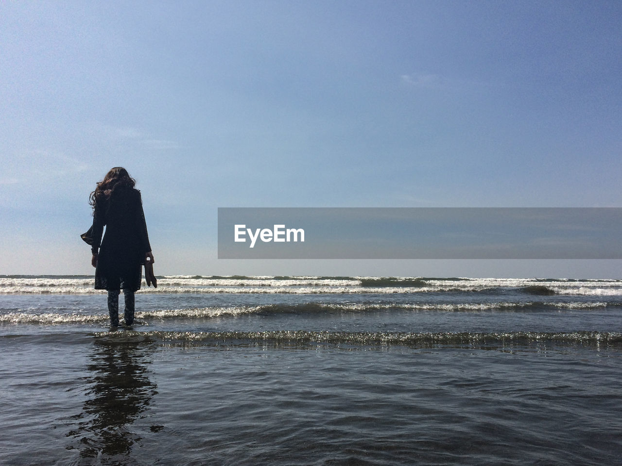 Rear view of woman standing on beach against sky