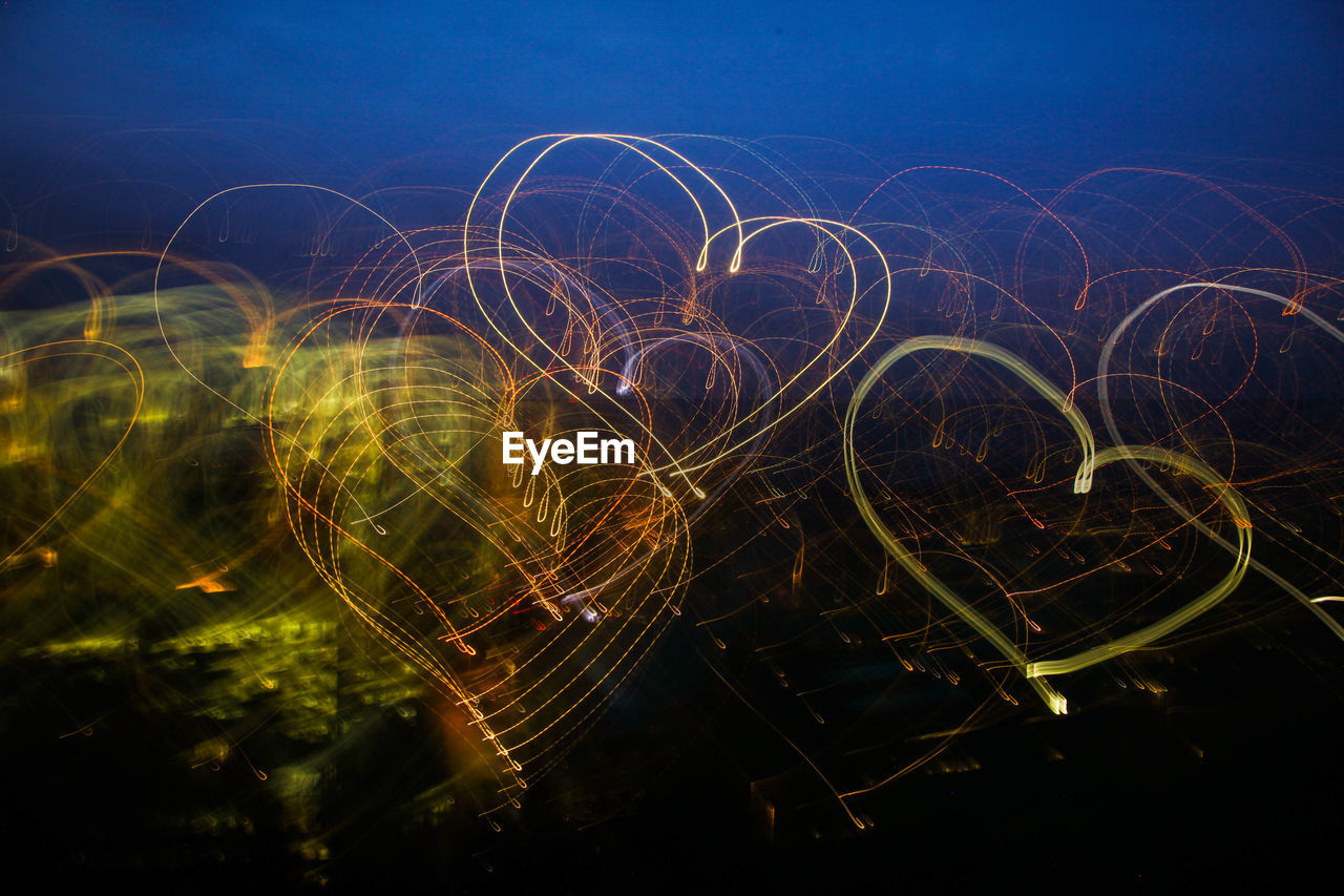 Close-up of heart shapes light trails against sky at night