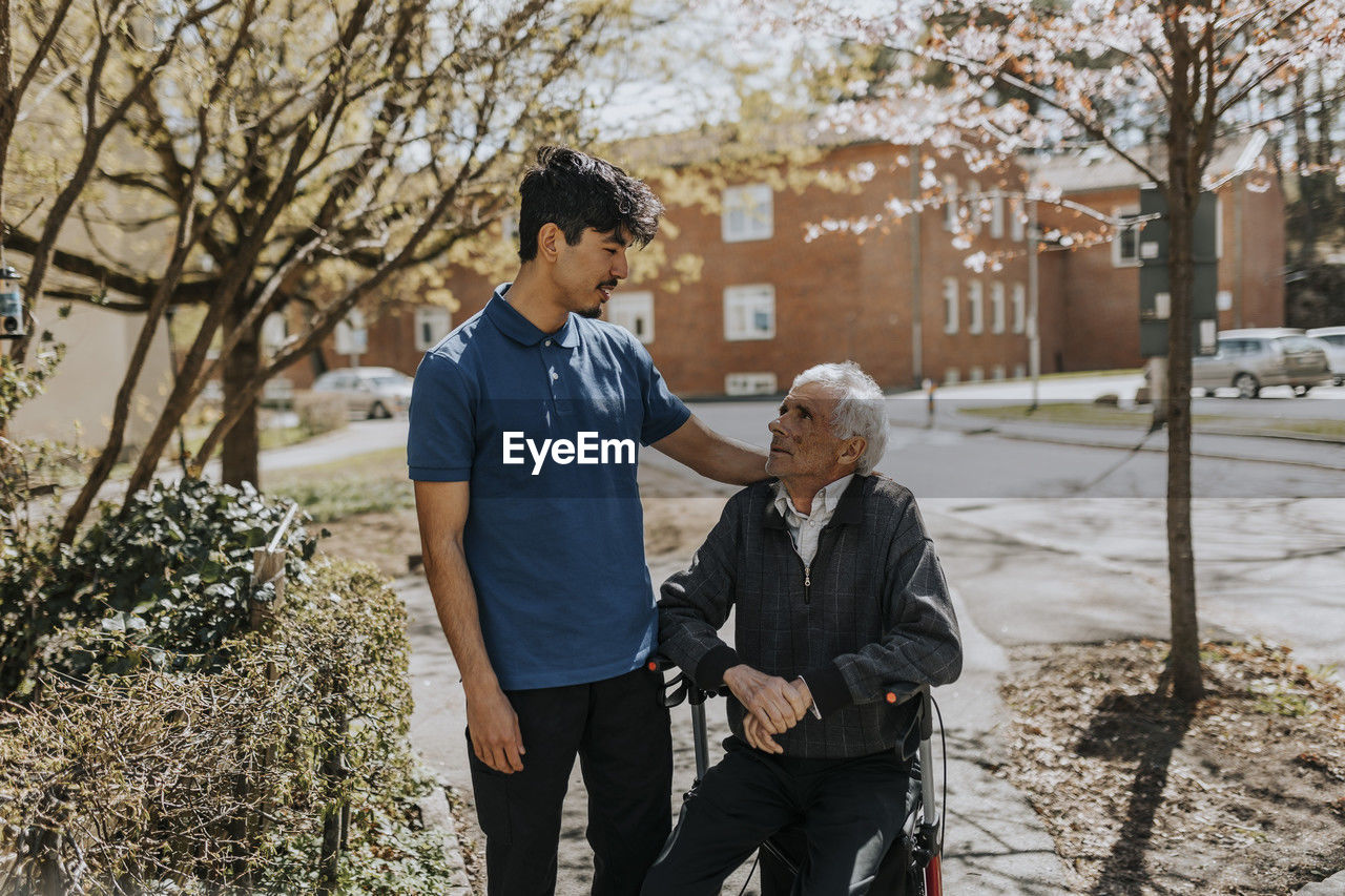 Male caregiver with hand on shoulder of senior man sitting on walker