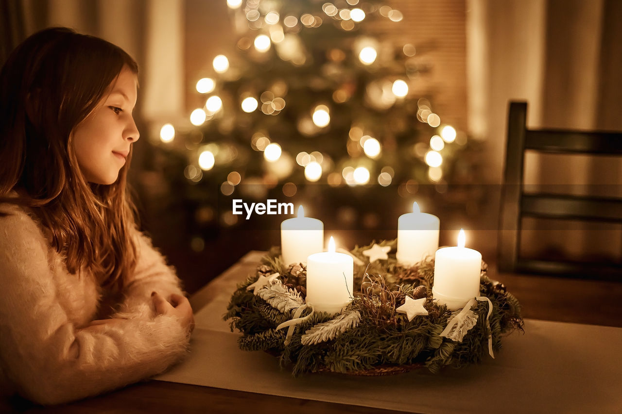 Child sits alone in front of a glowing advent wreath and looks forward to christmas