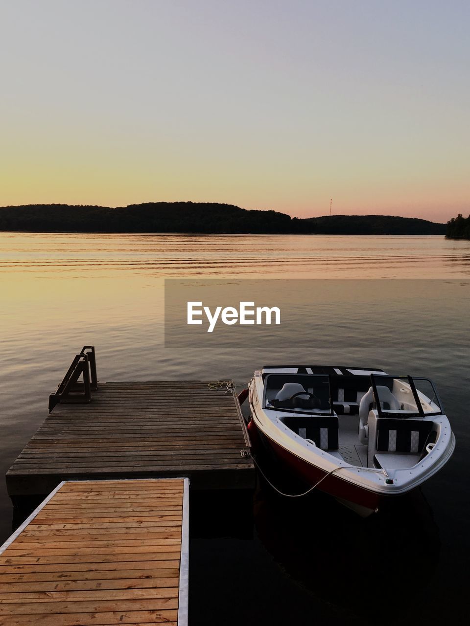 Boat moored in lake against sky during sunset