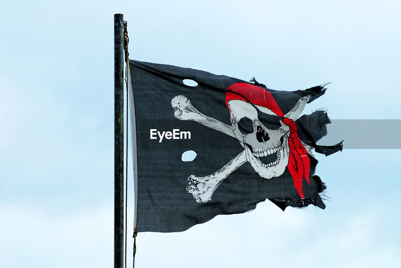Low angle view of torn pirate flag against sky