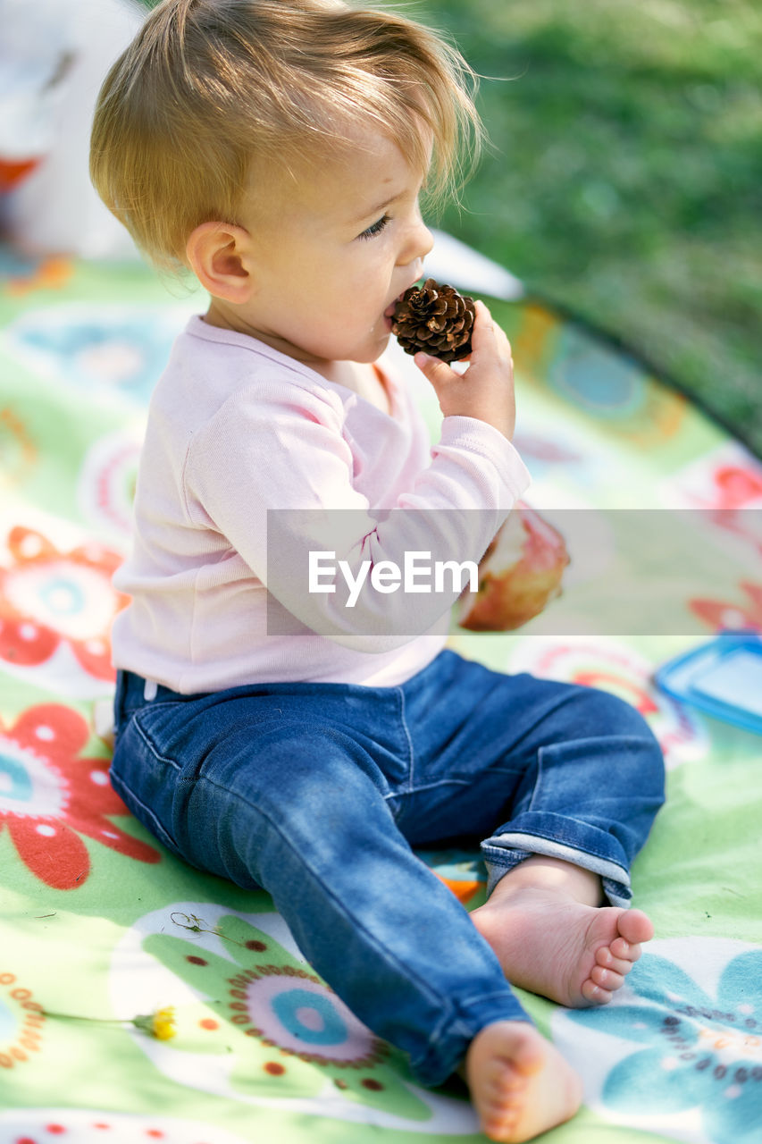 Cute baby girl eating food while sitting on grass outdoors