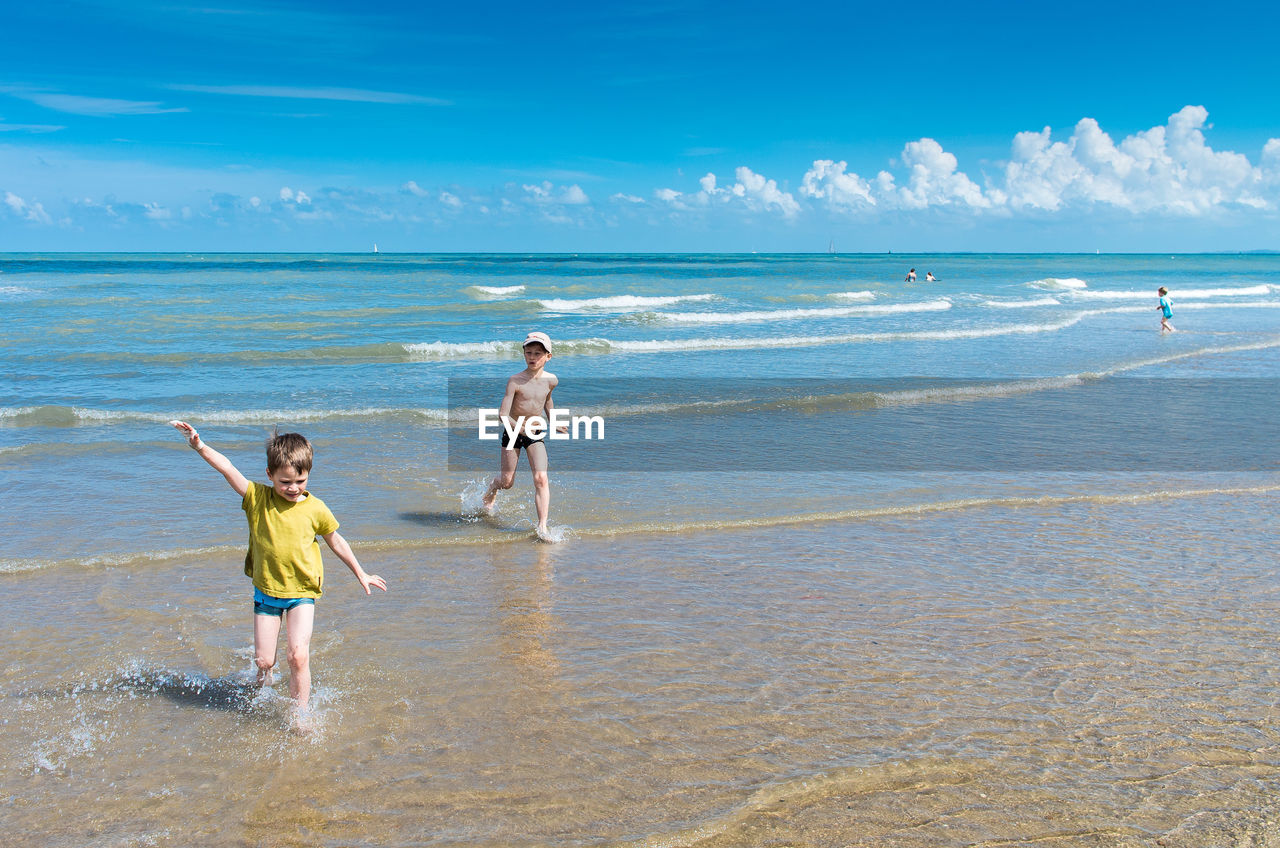 Siblings playing at beach against sky