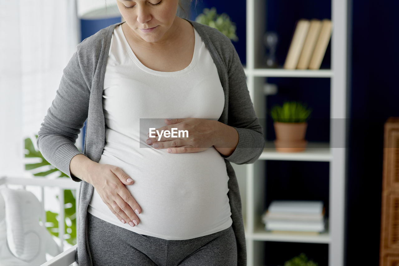 MIDSECTION OF WOMAN WEARING HAT STANDING AGAINST WALL