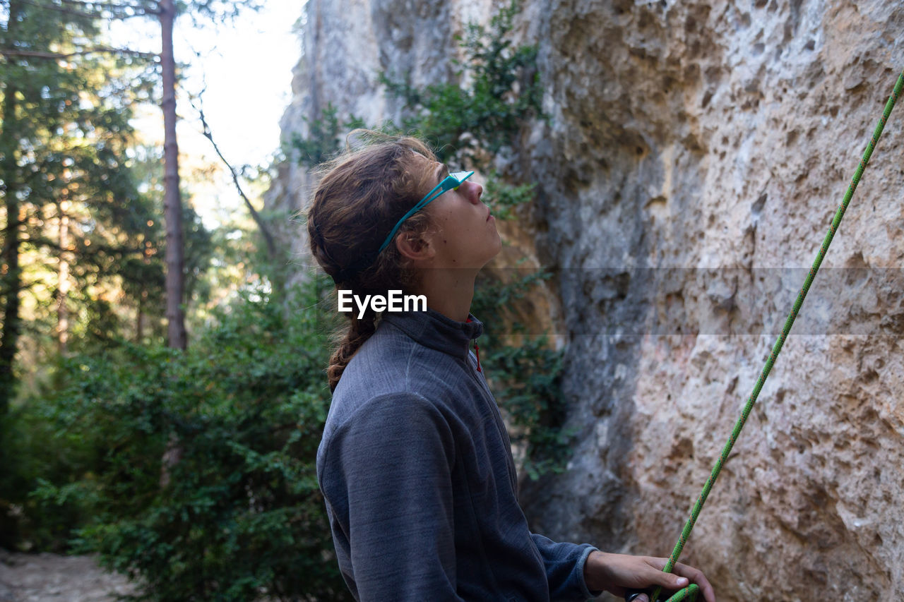 Side view of hiker holding rope while standing by rock